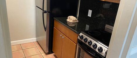 A compact kitchen with a refrigerator, oven, stove, and wooden cabinets.