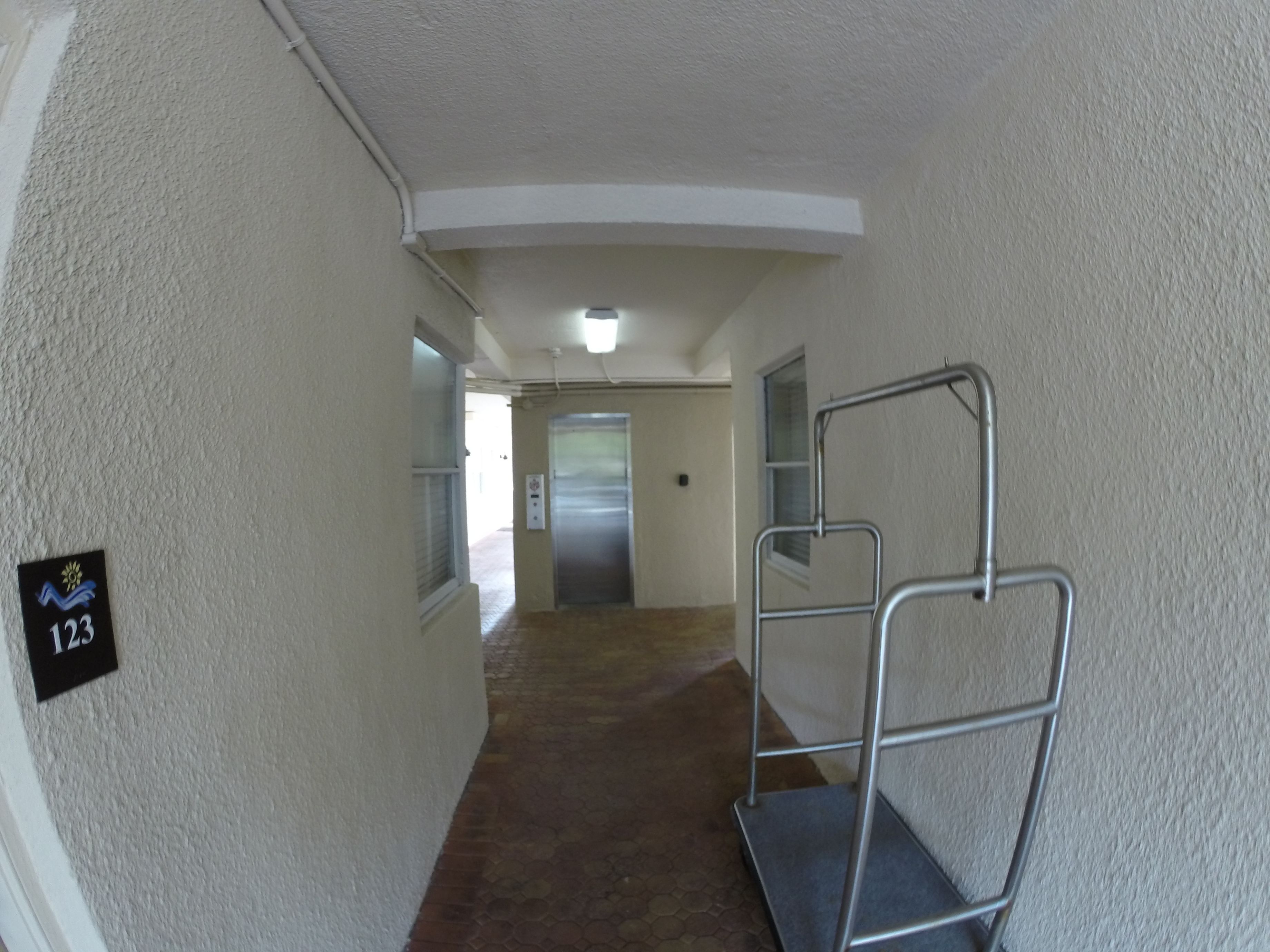 A narrow hallway with a metal handrail, a door at the end, and a sign with the number 123.