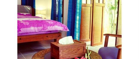 Una habitación con una cama, una mesita de noche de madera, una mesa redonda con una flor y una silla.