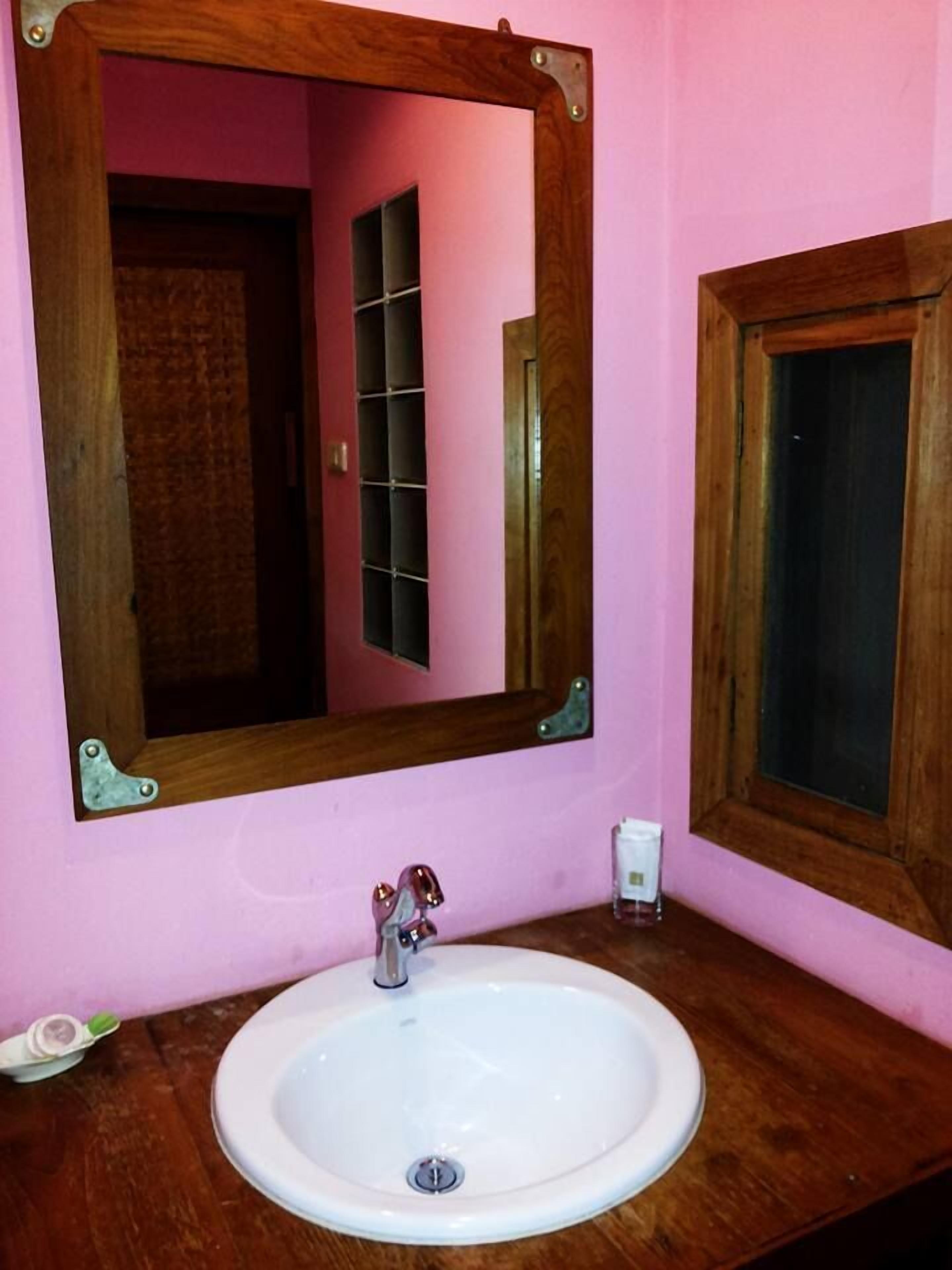 A bathroom with a wooden-framed mirror, a white sink, and a pink wall.