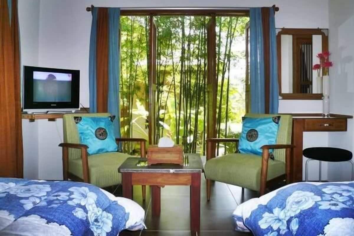 A room with two beds, a TV, a small table, and a window with a view of bamboo trees.