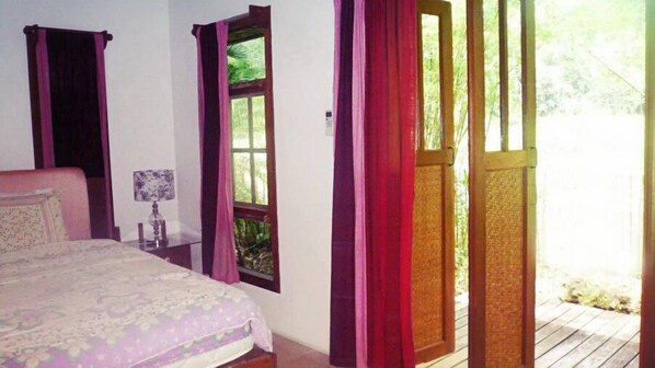 Un dormitorio con cama, mesita de noche, lámpara y ventana con cortinas.