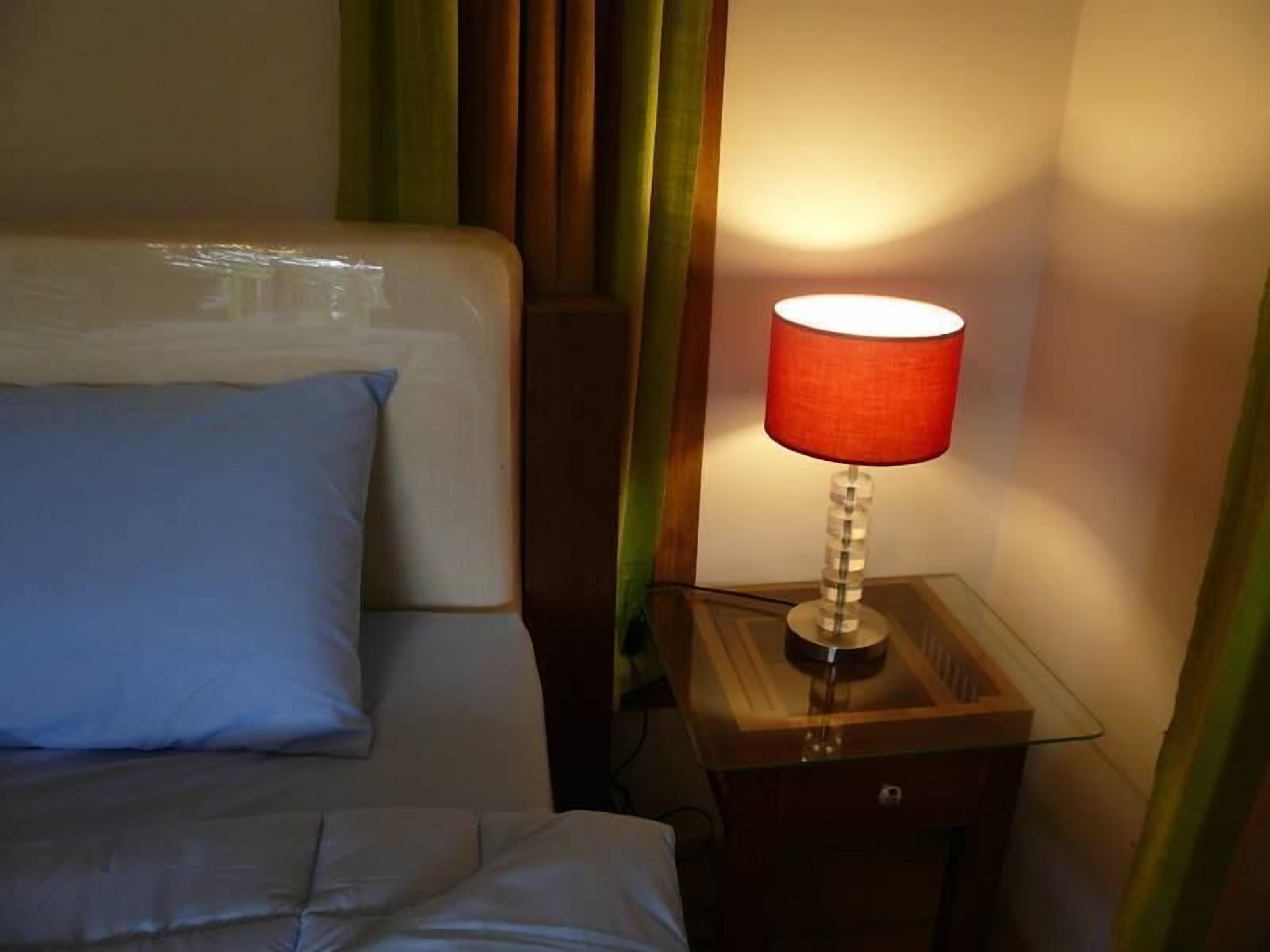 A bed with a blue pillow and a wooden nightstand with a red lamp.