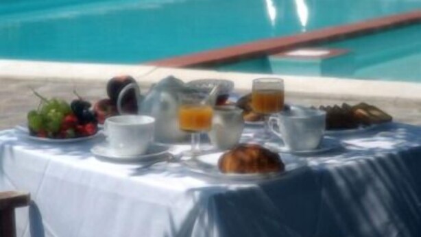 A breakfast setup by a pool with fruits, coffee, and juice.