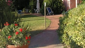 A pink villa with a garden, a pathway, and outdoor furniture.