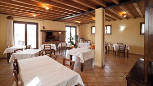 A dining area with multiple tables and chairs, wooden beams on the ceiling, and a fireplace.