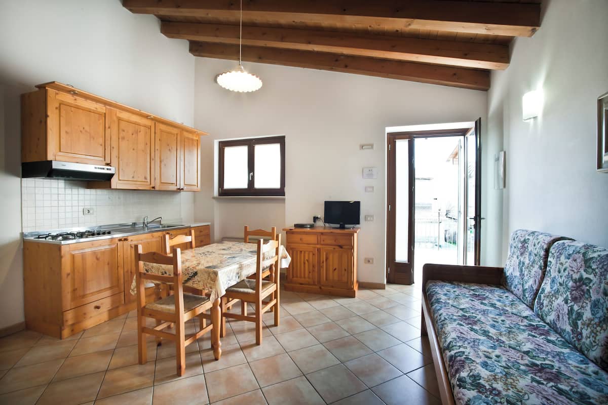A kitchen with wooden cabinets, a dining table with chairs, a sofa, and a television.