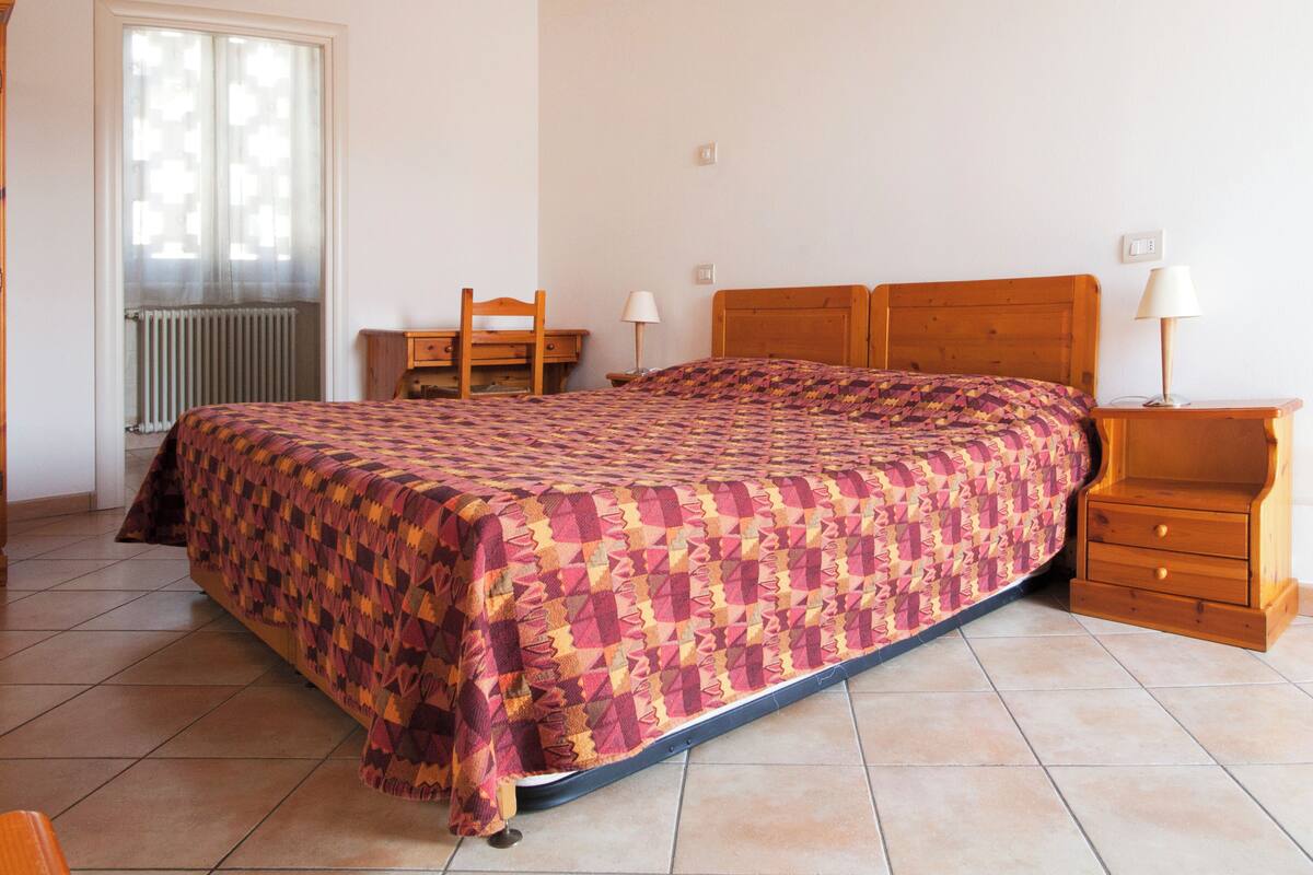 A bedroom with a bed, a chair, a nightstand, and a window.