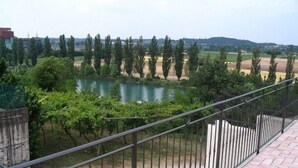 A balcony with a metal railing overlooking a river, surrounded by greenery and distant buildings.