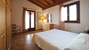 A bedroom with a wooden ceiling, a bed, a dresser, a chair, and a window with curtains.