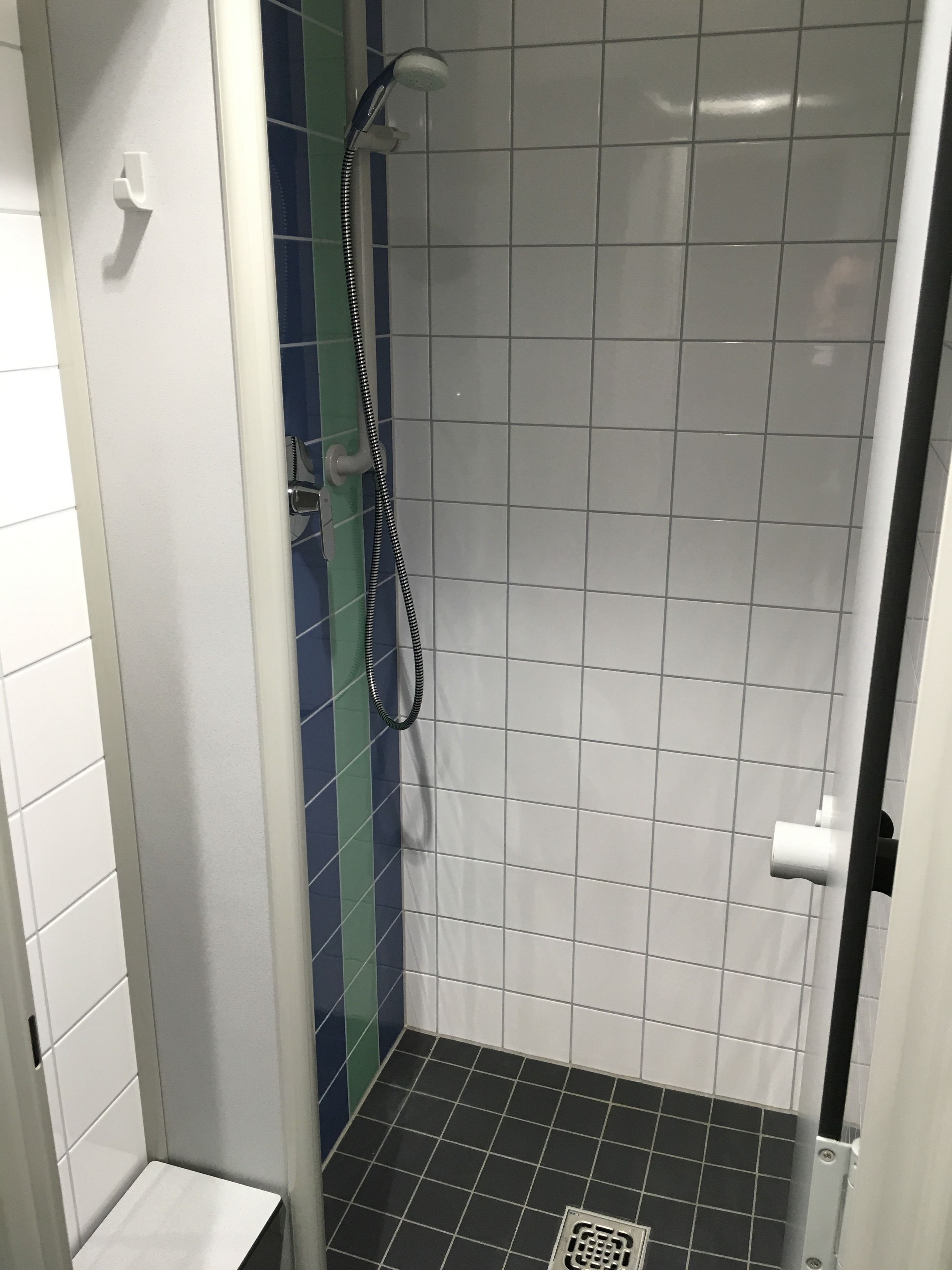 Un box de ducha pequeño con azulejos, un cabezal de ducha manual y desagüe.