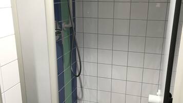 Un box de ducha pequeño con azulejos, un cabezal de ducha manual y desagüe.