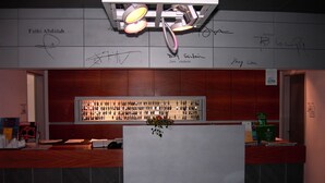 Un espace bar avec un comptoir, une étagère où sont exposées des bouteilles et un mur où sont apposées des signatures.