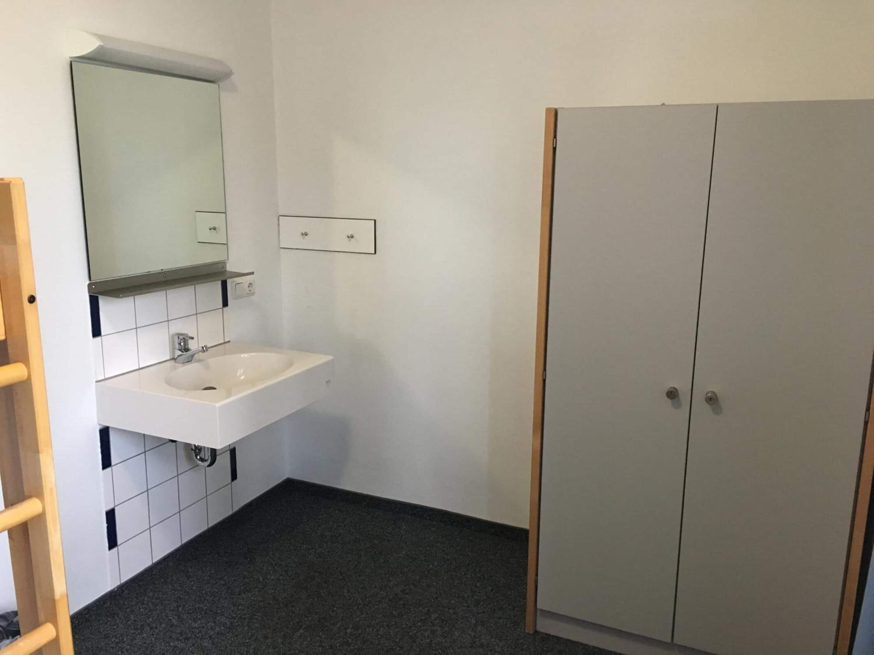 Un baño con lavamanos blanco, espejo y dos armarios.