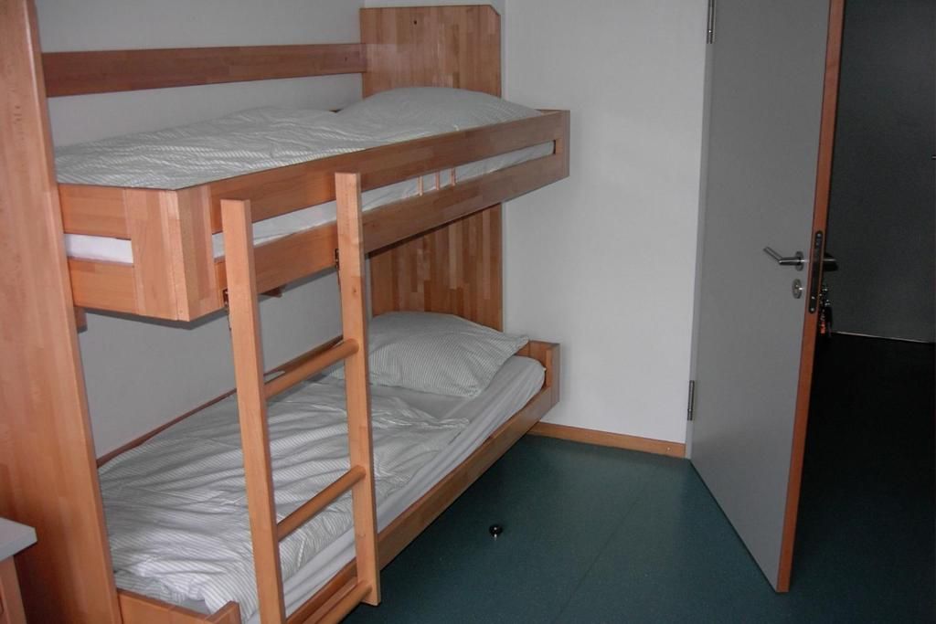 Une chambre avec un lit superposé, une porte et un petit objet noir sur le sol.