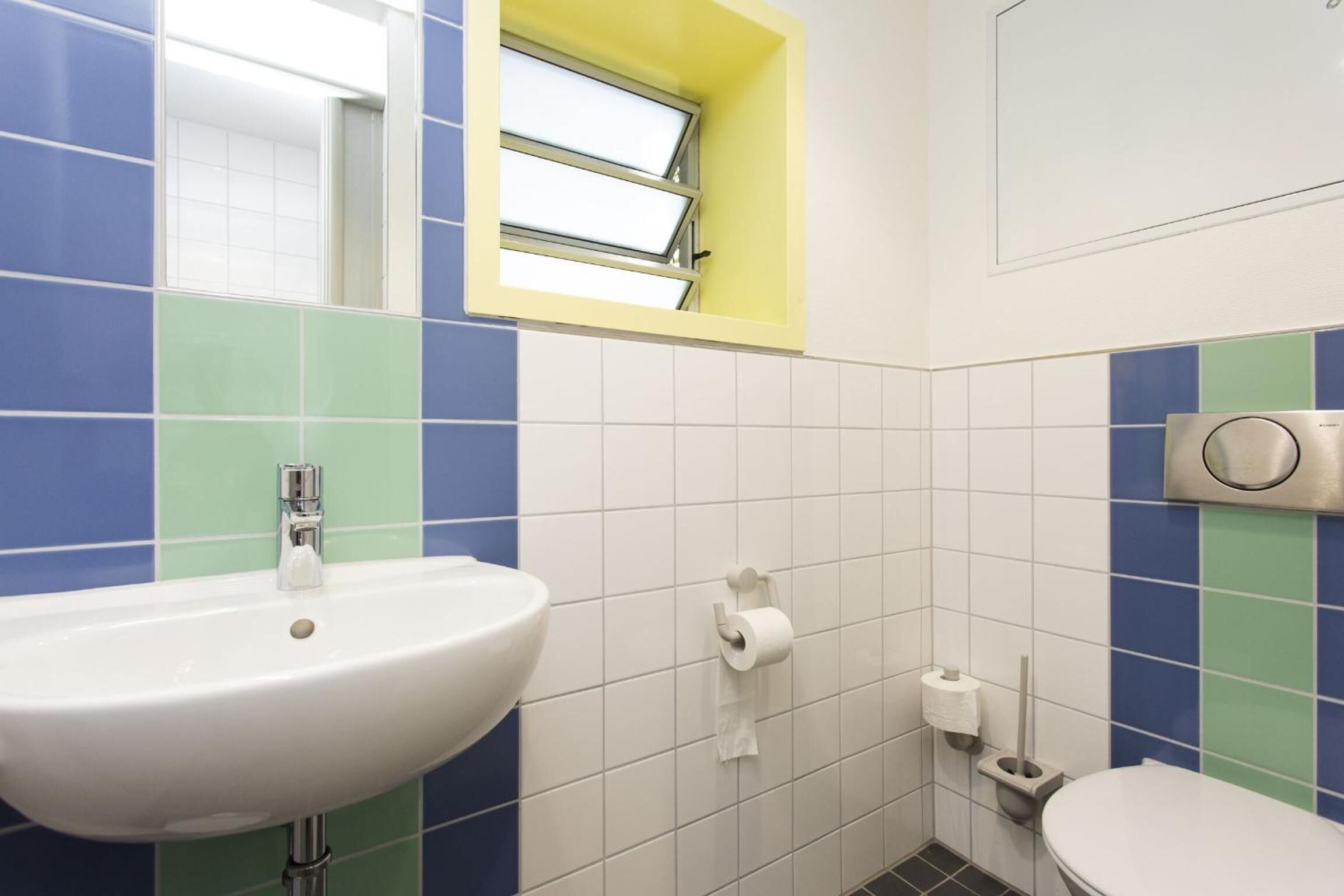 A bathroom with a white sink, a toilet, and a window with a yellow frame.