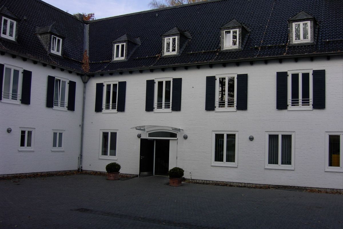 Un bâtiment blanc avec des volets noirs, une entrée centrale et de nombreuses fenêtres.
