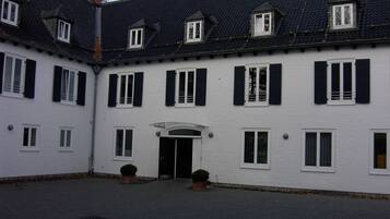 Un bâtiment blanc avec des volets noirs, une entrée centrale et de nombreuses fenêtres.