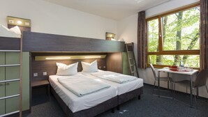 Une chambre avec un lit superposé, un bureau et une chaise, une fenêtre donnant sur les arbres et une échelle.