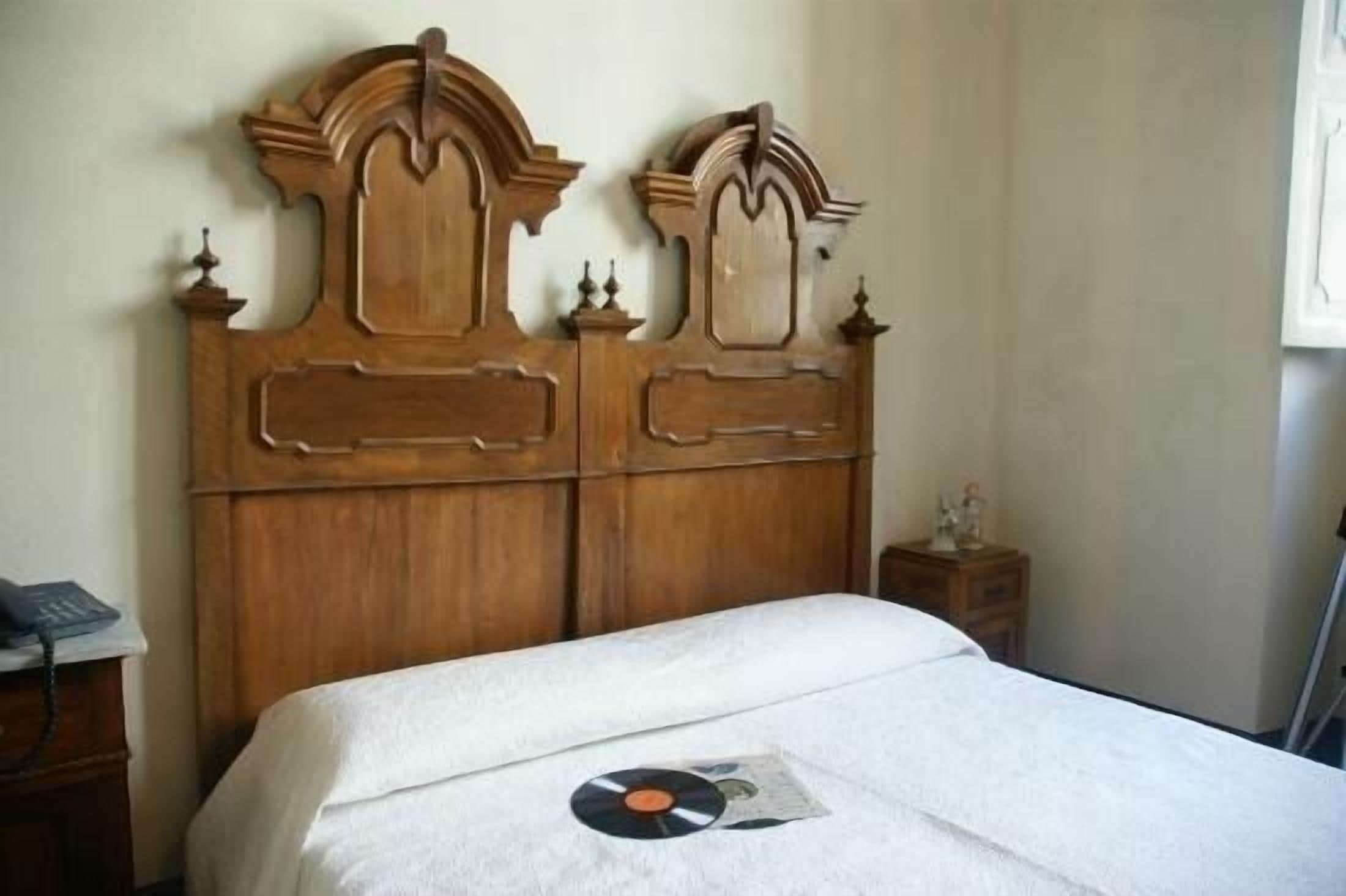 Una habitación con cabecera de madera, una cama con colcha blanca y una mesita de noche con teléfono.