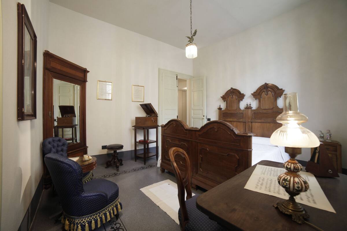 Ein Zimmer mit einem hölzernen Bett, einem Sessel, einem Tisch, einer Lampe und einem Spiegel.