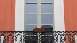Une façade d’immeuble dotée d’une grande fenêtre, de détails architecturaux travaillés et d’un balcon orné d’une balustrade en fer forgé.