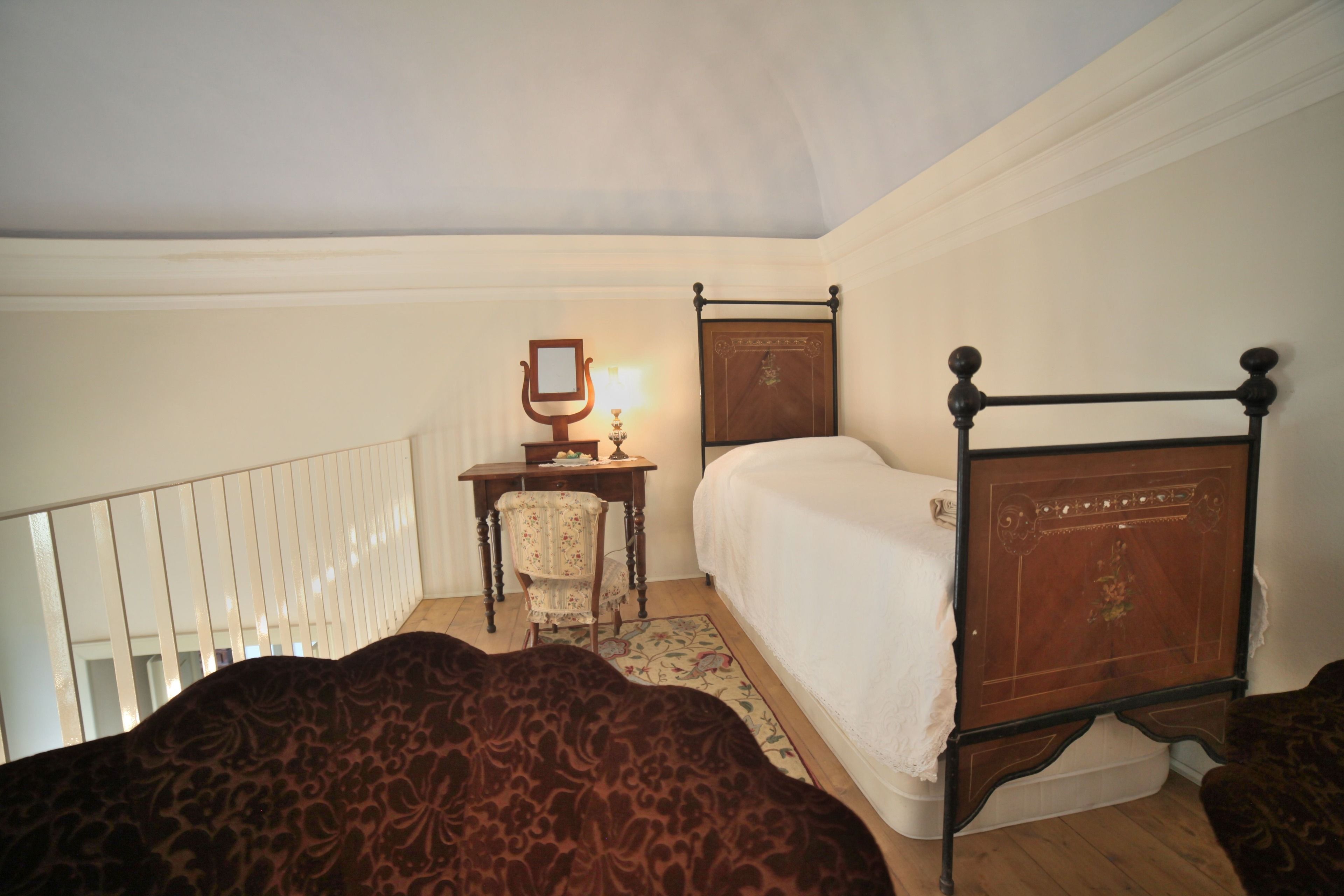 Un dormitorio con una cama de madera, una silla, un escritorio con espejo y una mesita de noche con lámpara.