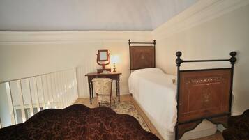A bedroom with a wooden bed, a chair, a desk with a mirror, and a small table with a lamp.