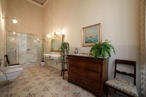 A bathroom with a marble sink, a wooden vanity, a chair, and a painting of a sailboat on the wall. - Residenza d'Epoca Regina d'Arborea (Oristano)