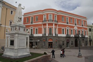 A building with a red facade and white trim, featuring a statue in front. - Residenza d'Epoca Regina d'Arborea (Oristano)