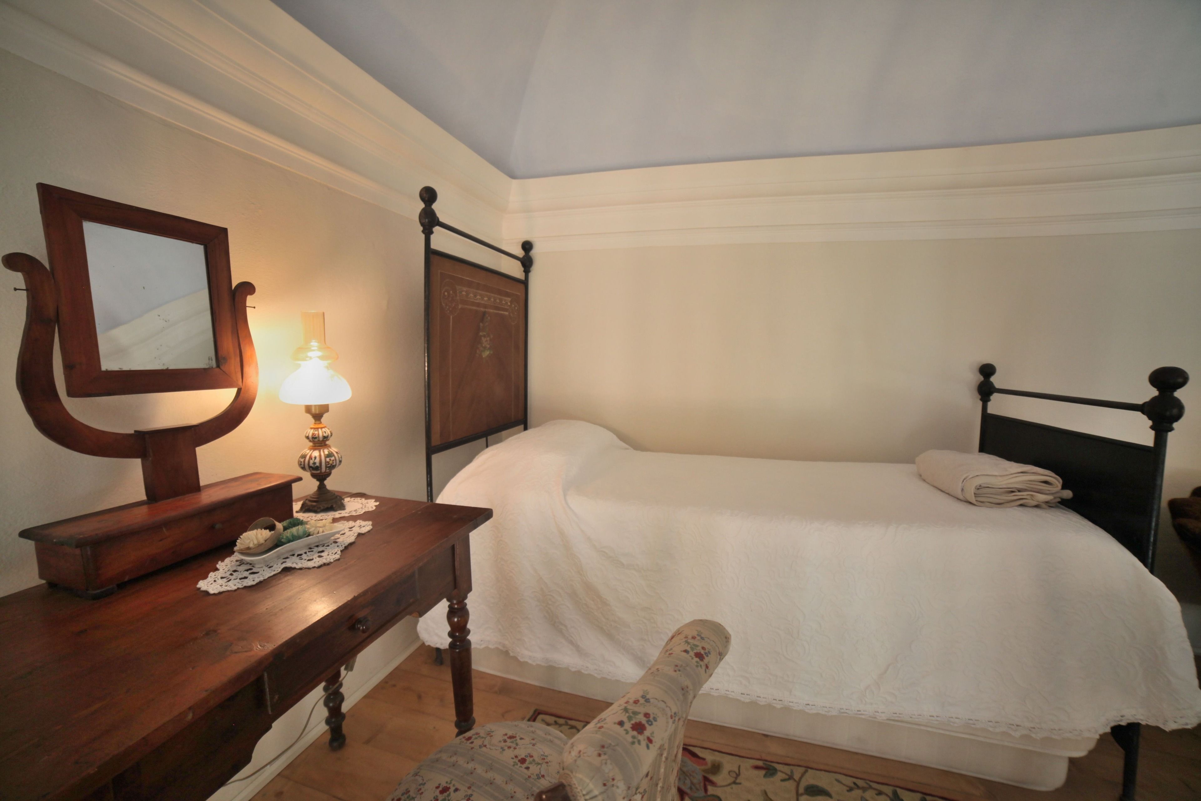 A bedroom with a wooden bed frame, a bedside table with a lamp, and a chair with a floral pattern.