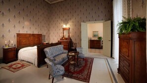 Une chambre à coucher de style traditionnel, avec un lit à baldaquin, un canapé recouvert d’un tissu bleu, une commode en bois et un tapis rouge à motifs.