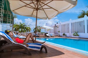 A poolside area with lounge chairs, umbrellas, and a clear blue pool.