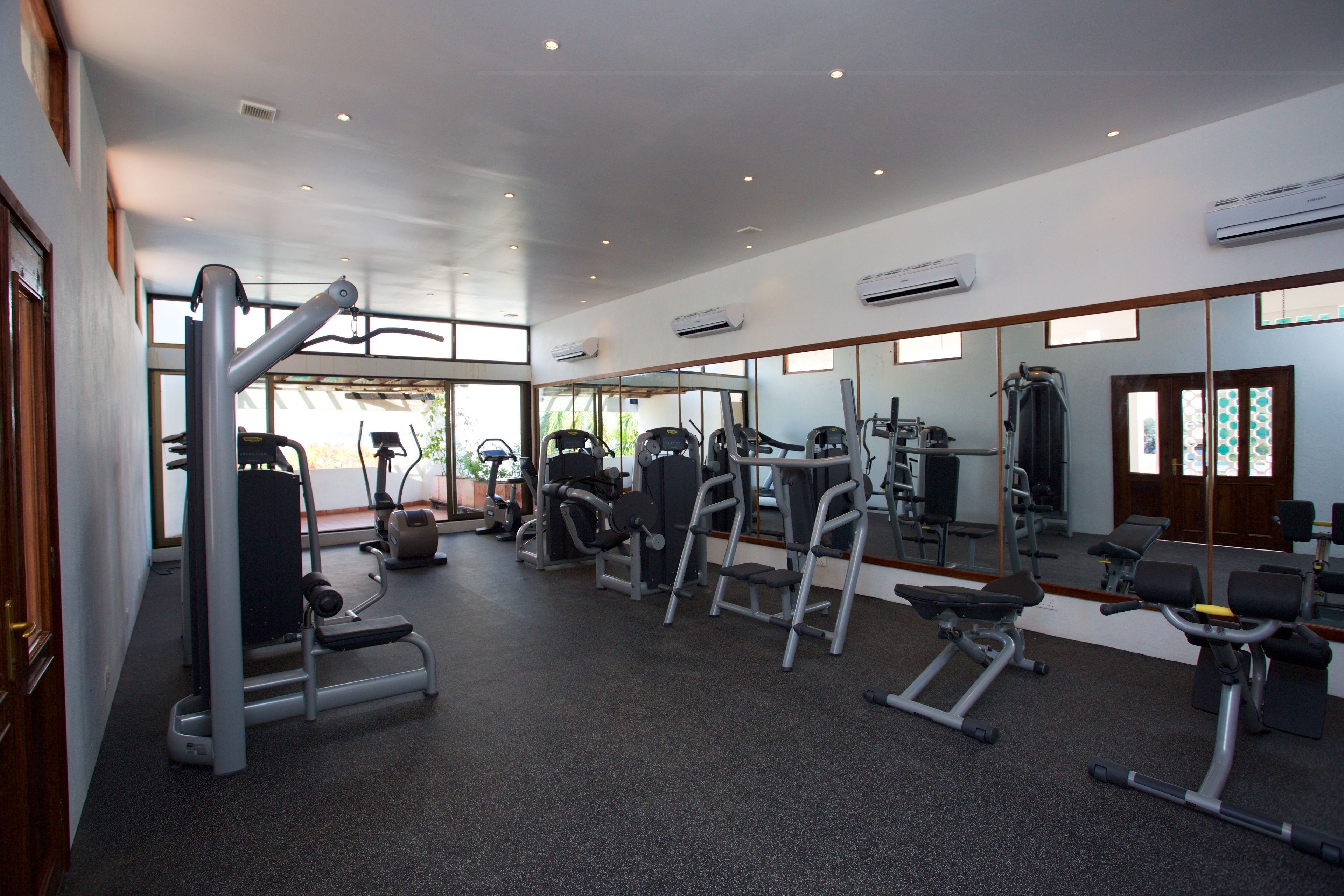 A gym with various exercise equipment, large windows, and an air conditioning unit on the ceiling.