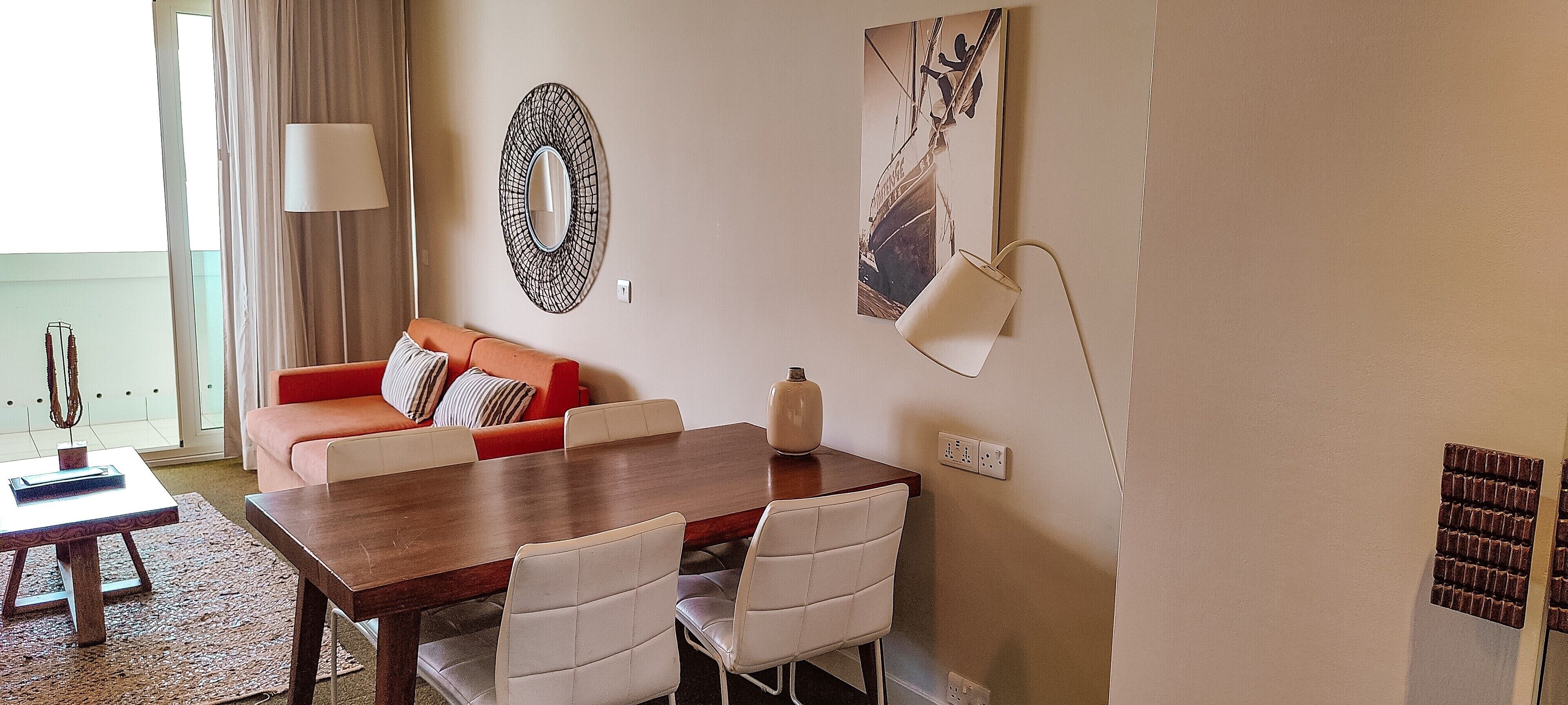 Un comedor con una mesa de madera, sillas blancas, un sofá rojo y una lámpara fijada a la pared.