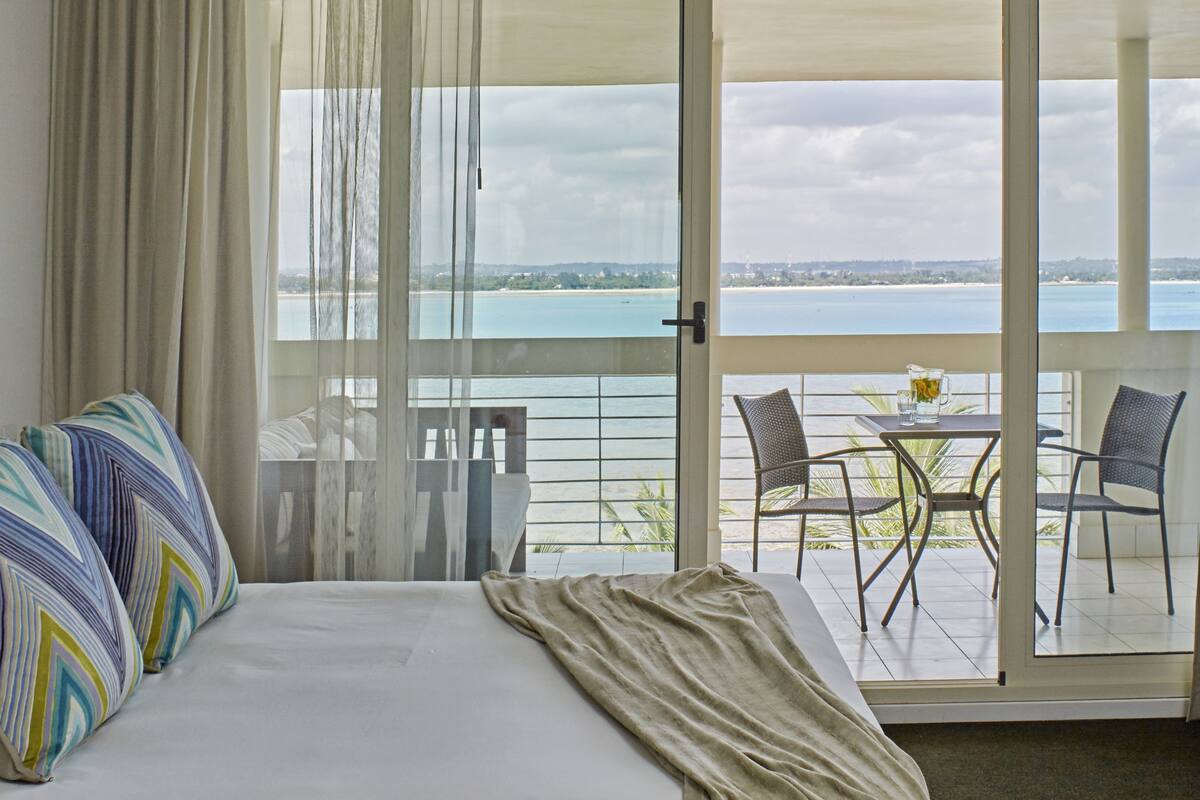 Ein Hotelzimmer mit Bett, Meerblick und einem Balkon mit Tisch und Stühlen.