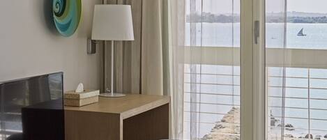 Habitación de hotel con televisión, lámpara y vistas al mar y a la playa.