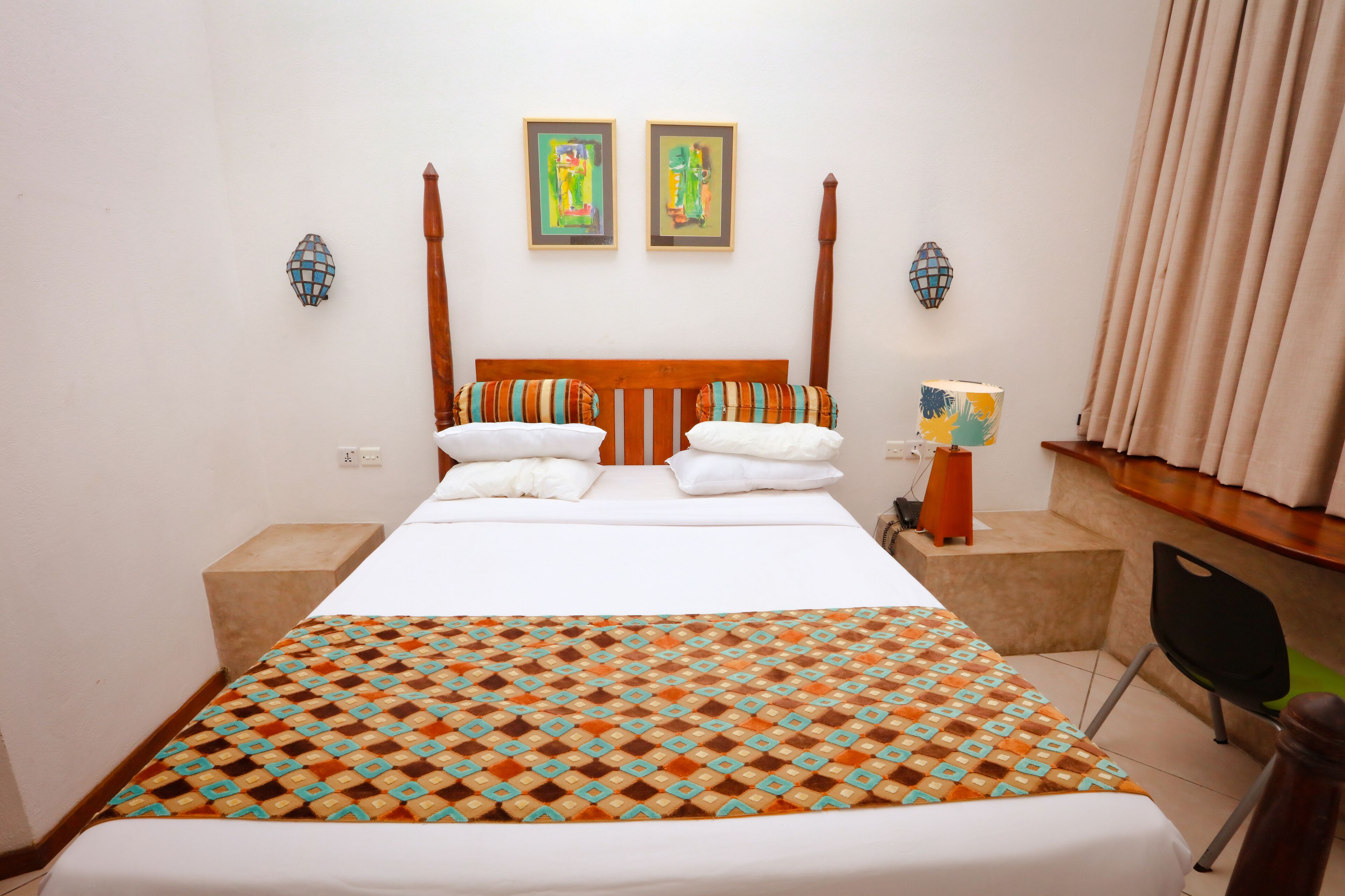 A hotel room with a bed, two paintings on the wall, a nightstand, a chair, and a lamp.