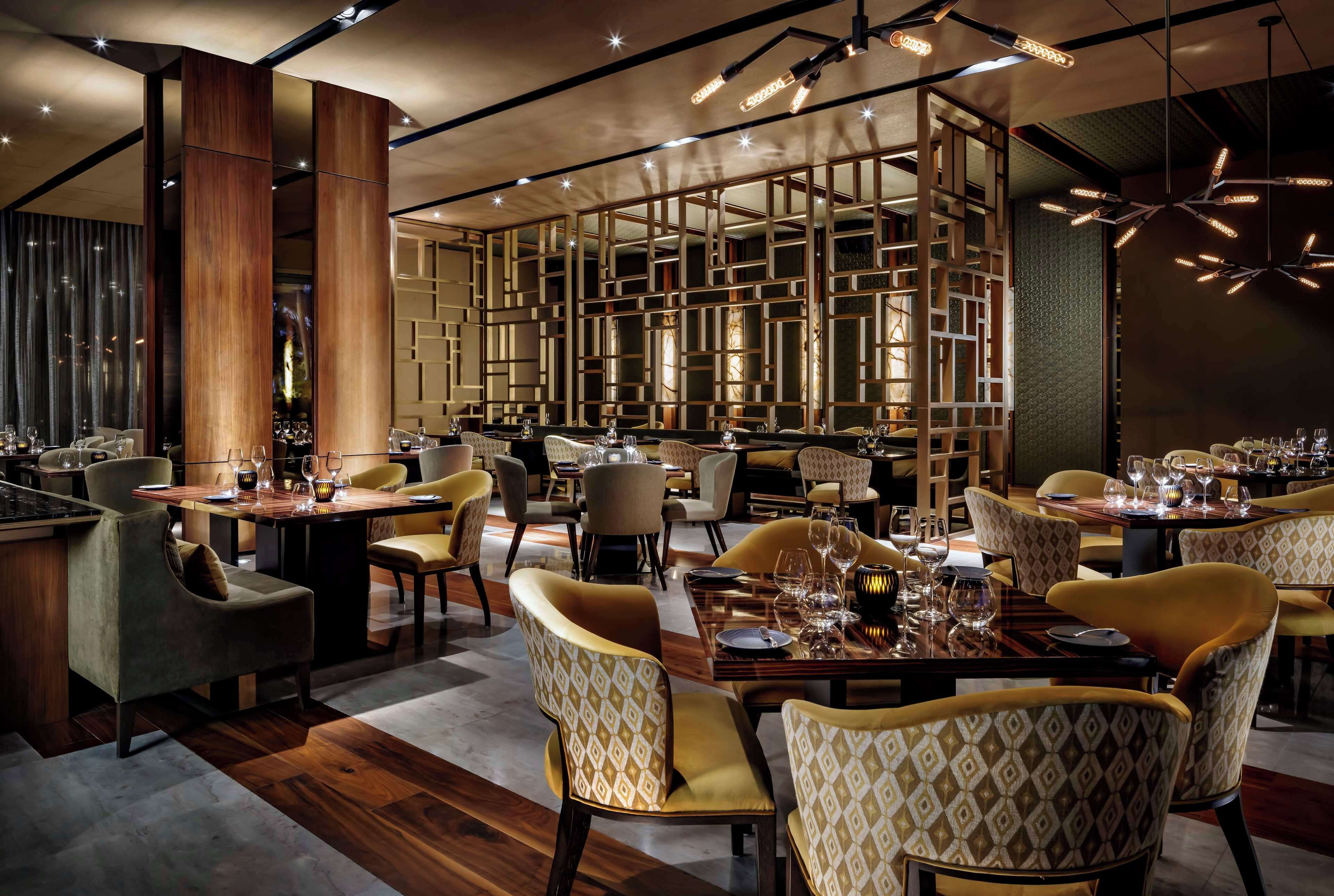Un restaurant moderne avec des boiseries, des chaises à motifs et des tables dressées pour le service.