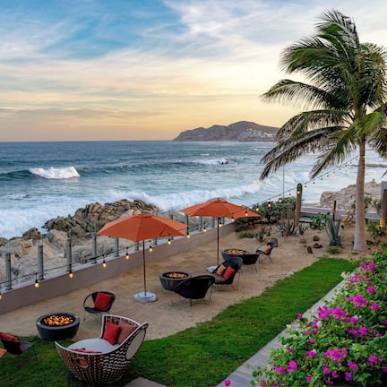 A coastal outdoor seating area with chairs, umbrellas, and a fire pit, overlooking the ocean.