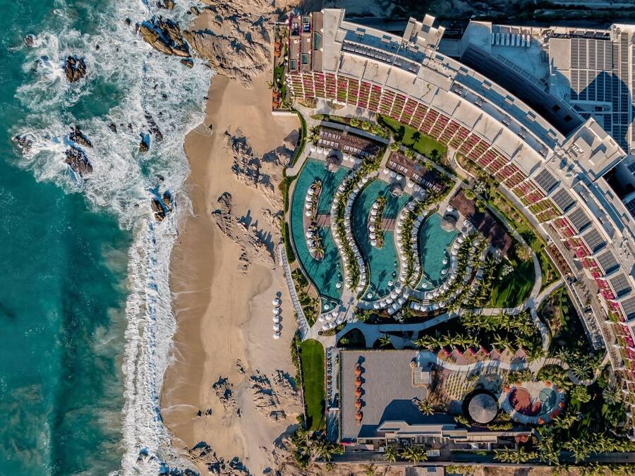 Vista aérea de un complejo turístico con varias piscinas, una playa y un estacionamiento.