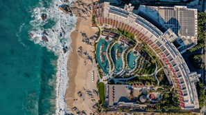 Vue aérienne d’un complexe hôtelier doté de plusieurs piscines, d’une plage et d’un parking.