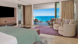 A modern hotel room with a large bed, a flat-screen TV, a balcony with a view of the sea, and a seating area with a table and chairs. - Grand Velas Los Cabos - All Inclusive (Cabo San Lucas)