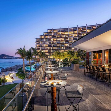 A rooftop bar with outdoor seating overlooking a beach and a hotel building.