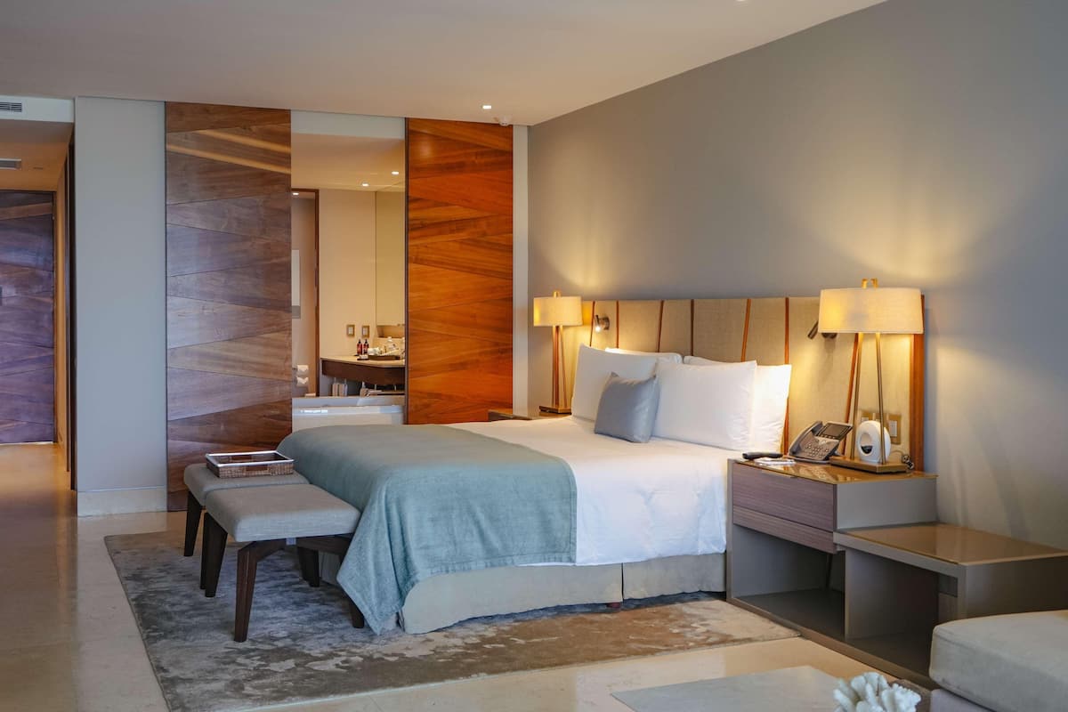 Habitación de hotel moderna con una cama grande, mesitas de noche, un espejo y un baño visible a través de una puerta abierta.