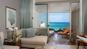 A modern living room with a sofa, a coffee table, and a view of the ocean through an open door. - Grand Velas Los Cabos - All Inclusive (Cabo San Lucas)