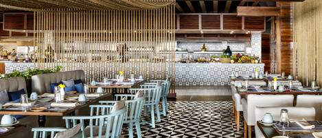 Un restaurante con piso de diseño geométrico, sillas azul claro y una zona de bar central con salpicadero de azulejos.