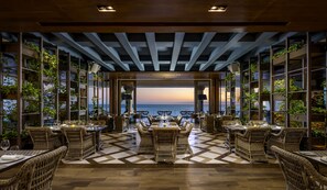 A restaurant with a checkered floor, wicker furniture, and shelves with plants. - Grand Velas Los Cabos - All Inclusive (Cabo San Lucas)