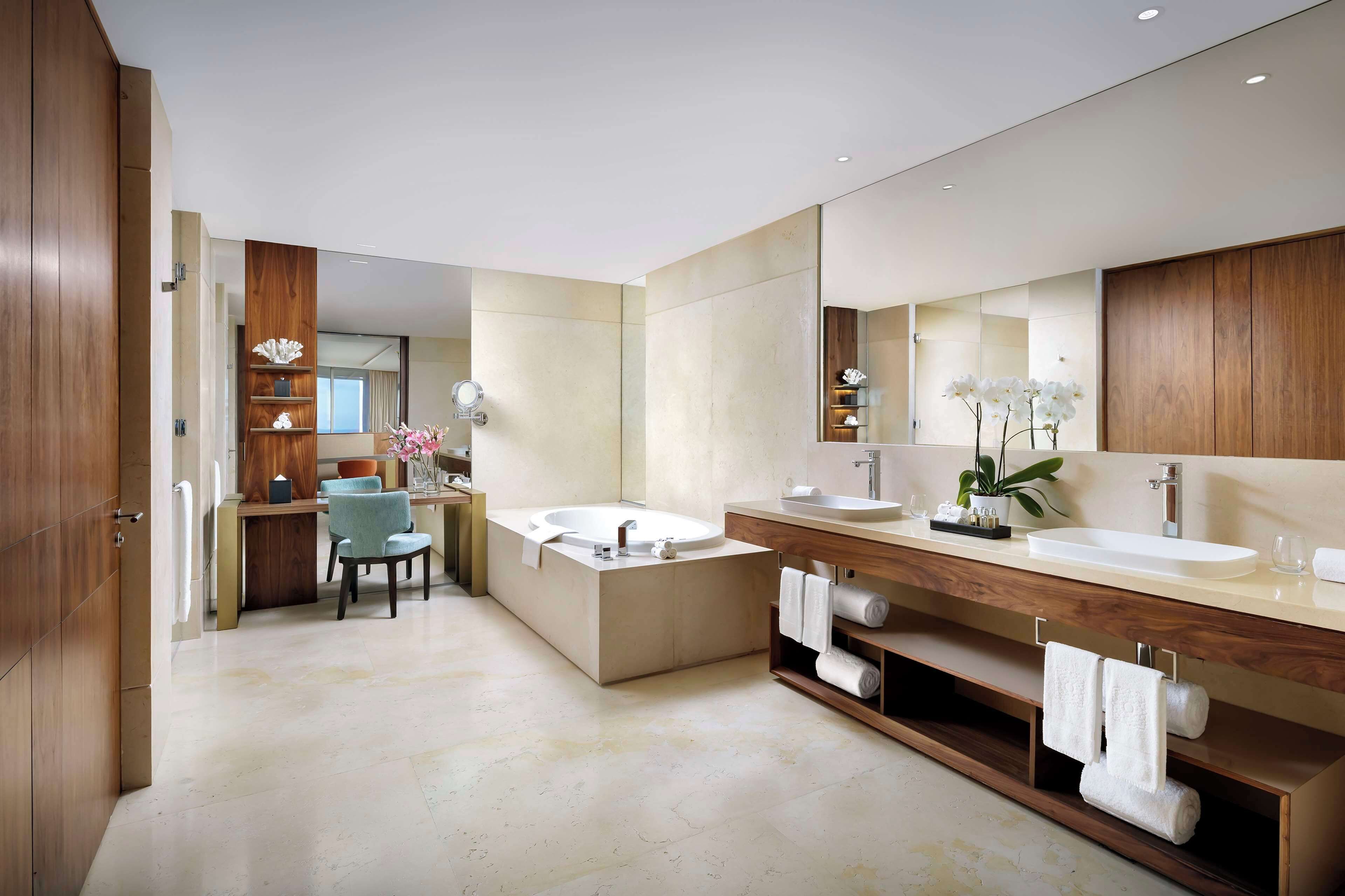 A modern bathroom with a large bathtub, two sinks, a vanity, and a mirror.