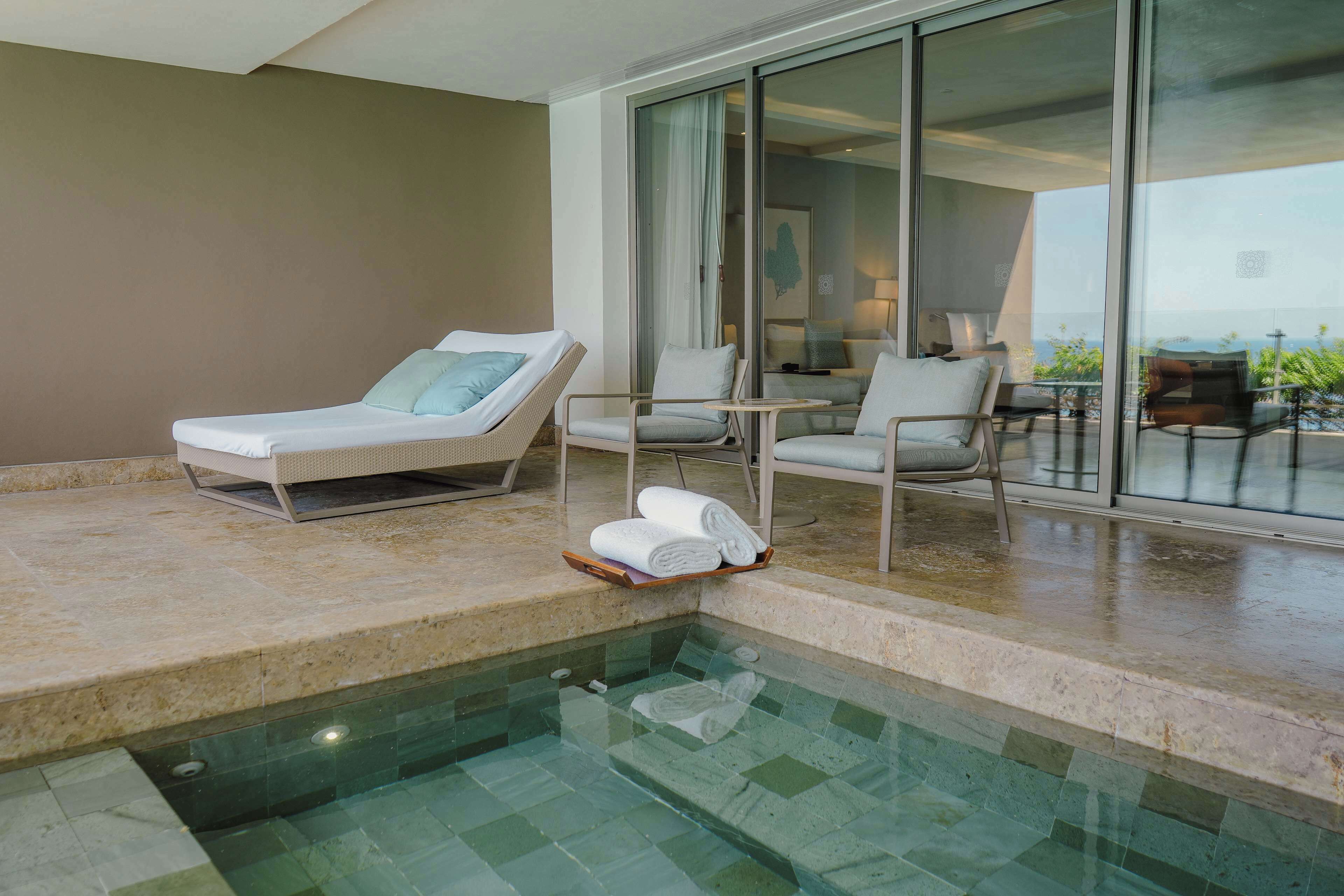 A poolside area with lounge chairs, a glass-enclosed balcony, and a view of the landscape.